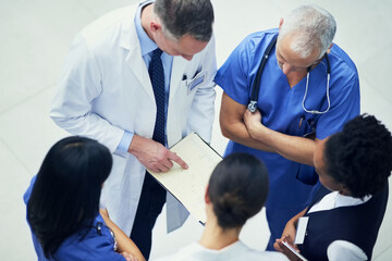 Discussing diagnoses. Shot of a group of doctors talking together over a medical chart while standing in a hospital.