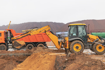 An excavator loads soil or sand into a dump truck. Pit development. Earthworks with the help of heavy construction equipment.