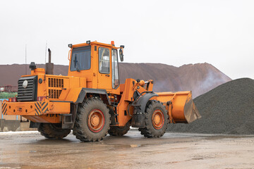 The front loader picks up gravel or crushed stone in the front bucket. Heavy construction machinery at the construction site. Transportation of materials at a concrete plant.