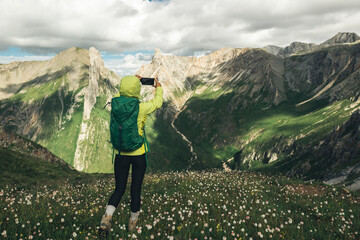 Successful woman backpacker using smartphone taking photo hiking on alpine mountain top