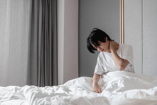young man sitting on the bed with hands covering his neck