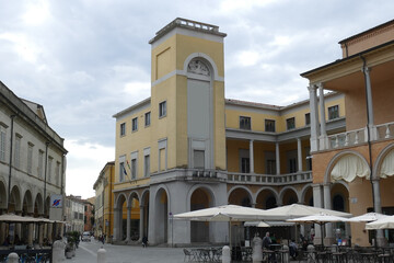 Fototapeta na wymiar piazza del popolo in Faenza surrounded by palaces with cafe, shops and the yellow tower in the background