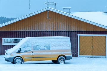 Yellow Ford Transit van covered in snow in front of a colored door of barn in Finland