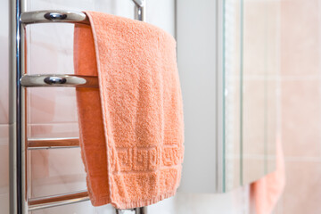orange terry towel hanging on a chrome heated towel rail in the bathroom