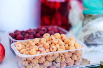 Agricultural industry. Street trade. Traditional fair. Yellow raspberries in a transparent box. Ripe cranberry berries in the background. Daytime. Selective focus.