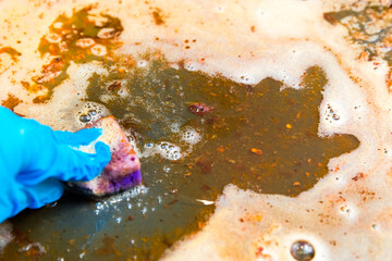 Gloved hand washes dirty greasy baking sheet with a sponge