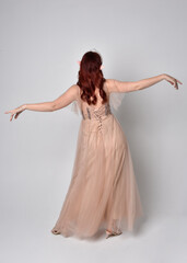 Full length portrait of pretty female model with red hair wearing glamorous fantasy tulle gown and...
