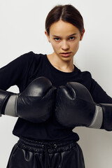 young woman in boxing gloves in black pants and a T-shirt light background