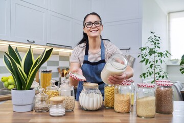 Smiling woman in the kitchen with jars of stored food. - obrazy, fototapety, plakaty