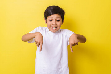 Happy little boy with pointing down gesture isolated on yellow background