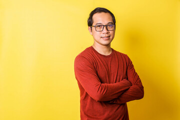 Thoughtful casual man in glasses folding hands looking at camera isolated on yellow background