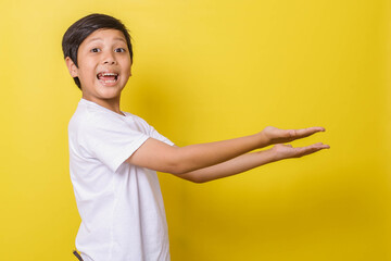 Cheerful little boy smiling with sideways presentation gesture isolated on yellow background