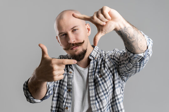 Closeup of creative bald bearded photographer who making frame with fingers in front of face 