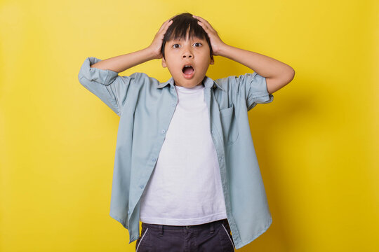 Surprised little boy holding head with both hands isolated on yellow background. omg's expression 