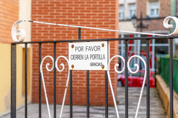 A metal sign on the gate with an ornate iron pattern at the entrance courtyard, with an inscription...