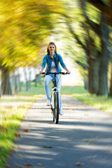 young slender blonde woman in jeans rides a bike in a summer park