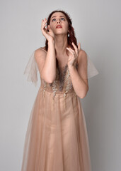 portrait of pretty female model with red hair wearing glamorous fantasy tulle gown and crown. ...