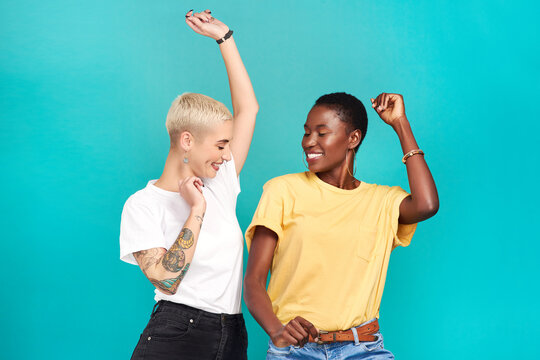 Grab Your Girl And Get Grooving. Studio Shot Of Two Young Women Dancing Together Against A Turquoise Background.