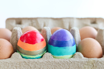 Rainbow Easter eggs surrounded of many eggs in carton cage, colorful eggs painted in rainbow colors of LGBTQ gays and lesbians flag in cardboard box with other eggs, symbol of diversity in harmony.