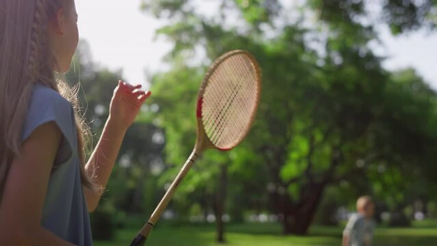Bored girl play badminton with brother touching racket net in park. Rear view