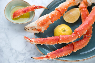 Closeup of boiled legs and claws of kamchatka crab served on a turquoise plate, horizontal shot on a light-grey marble surface