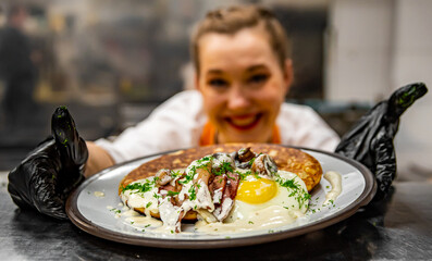 Chef's hands in gloves cooking fried pancake with mushroom sauce, bacon and egg on kitchen