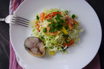 Beautiful healthy gourmet salad of cabbage and vegetables. Piece of fish on a white plate.