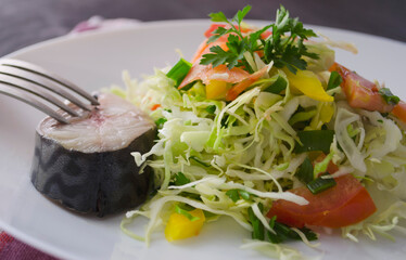 Beautiful healthy gourmet salad of cabbage and vegetables. Piece of fish on a white plate.