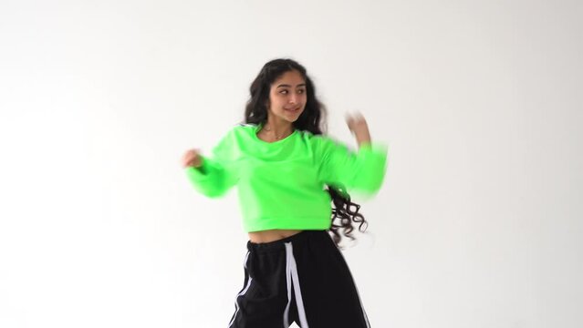 Young happy mixed race woman with black long hair dancing modern dance against a white wall background. Street dance.
