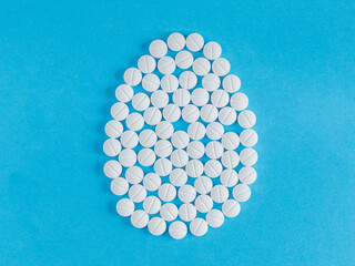 Creative flat lay composition with easter egg shape made of medical pills on blue background. Pastel color and soft shadows. Realistic aesthetic look. Contemporary style Copy space, top view, flat lay