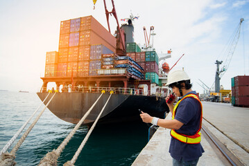 Engineers and crane.smiling dock worker holding radio and Container ship under bridge crane in port background.