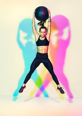 Fototapeta na wymiar Strong woman does exercise med ball slams with jump. Photo of woman with perfect physique on white background with effect of rgb colors shadows. Strength and motivation.