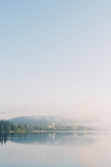The village and lake Titisee Neustadt in Baden-W&uuml;rttemberg in Germany. Foggy blue lake in the morning with forest, church and town in the clouds