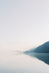 Lake Titisee Neustadt in Baden-W&uuml;rttemberg in Germany. Blue lake with morning fog with mountains in shadow in the clouds