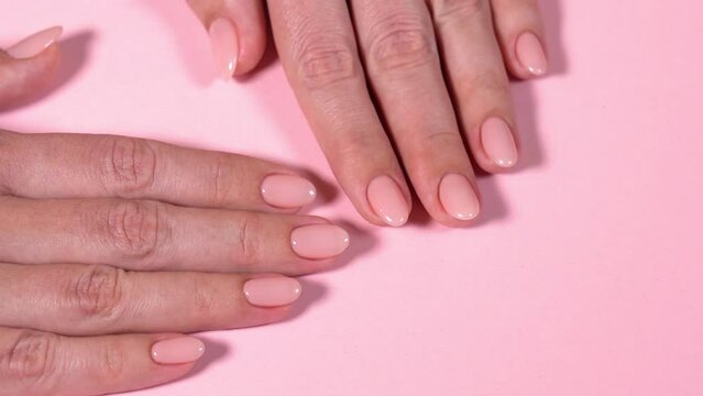 Closeup top view full hd video footage of elegant pastel pink natural manicure. Female hands isolated on pink pastel color texture background. Pink professionally manicured nails of european woman