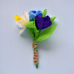 a small bouquet of spring flowers of narcissus and crocuses made of corrugated paper on a blue background a gift for mom