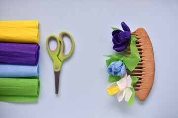 diy spring flowers from crepe paper on a blue background with scissors and paper and a wooden scallop