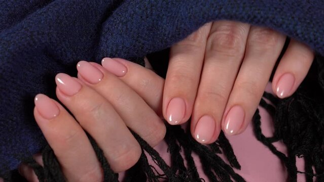 Closeup top view full hd video footage of elegant pastel pink natural manicure. Female hands isolated on fluffy dark blue knitted fabric texture background