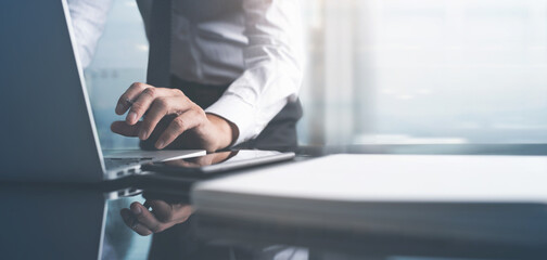 Businessman busy working on laptop computer, surfing the internet with document on table at modern office with blurred copy space