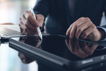 Businessman using stylus pen signing e-document on digital tablet with laptop computer on table at office, e-signing, electronic signature, paperless office