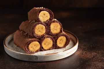stack of vegan chocolate crepes with banana and chocolate spread filling on dark background. Chocolate pancakes for breakfast