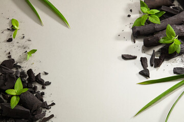Flatlay of bamboo activated charcoal and charcoal powder decorate with green leaf in white background  - obrazy, fototapety, plakaty