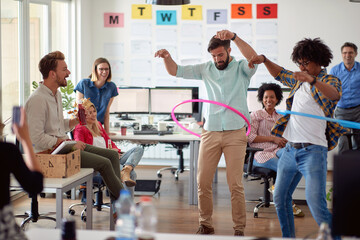 Two male employees is playing with hula-hoop in the office with their colleagues. Employees, job, office - obrazy, fototapety, plakaty