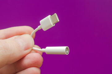 white adapter cable type-c to audio 3.5 in hand on a purple background - obrazy, fototapety, plakaty