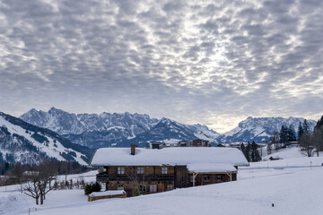 Fototapeta na wymiar wooden house, cabin in the snow with mountains and nice cloudy sky during sunset