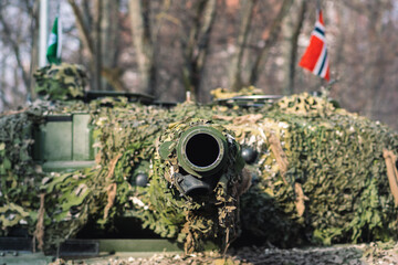 Norwegian Army armored tank with cannon and camouflage coating with flag of Norway and trees on...