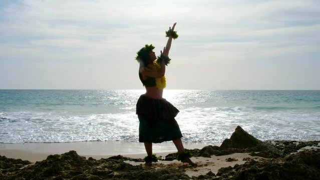 Pretty and energetic woman performing hawaiian dancing on the beach with blanks. The perfect landscape. Silhouette.