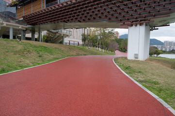 The red asphalt runway in the modern city park is surrounded by green plants on both sides