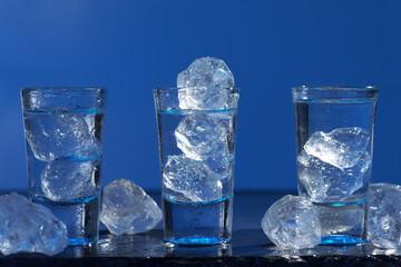 Glass of vodka with ice on blue background, selective focus