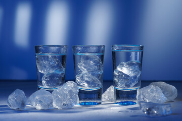 Glass of vodka with ice on blue background, selective focus